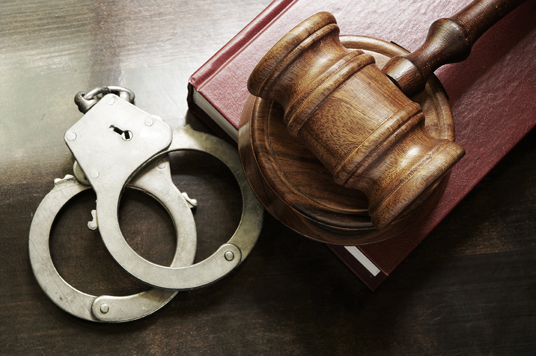Gavel and handcuffs with red legal book on wooden table